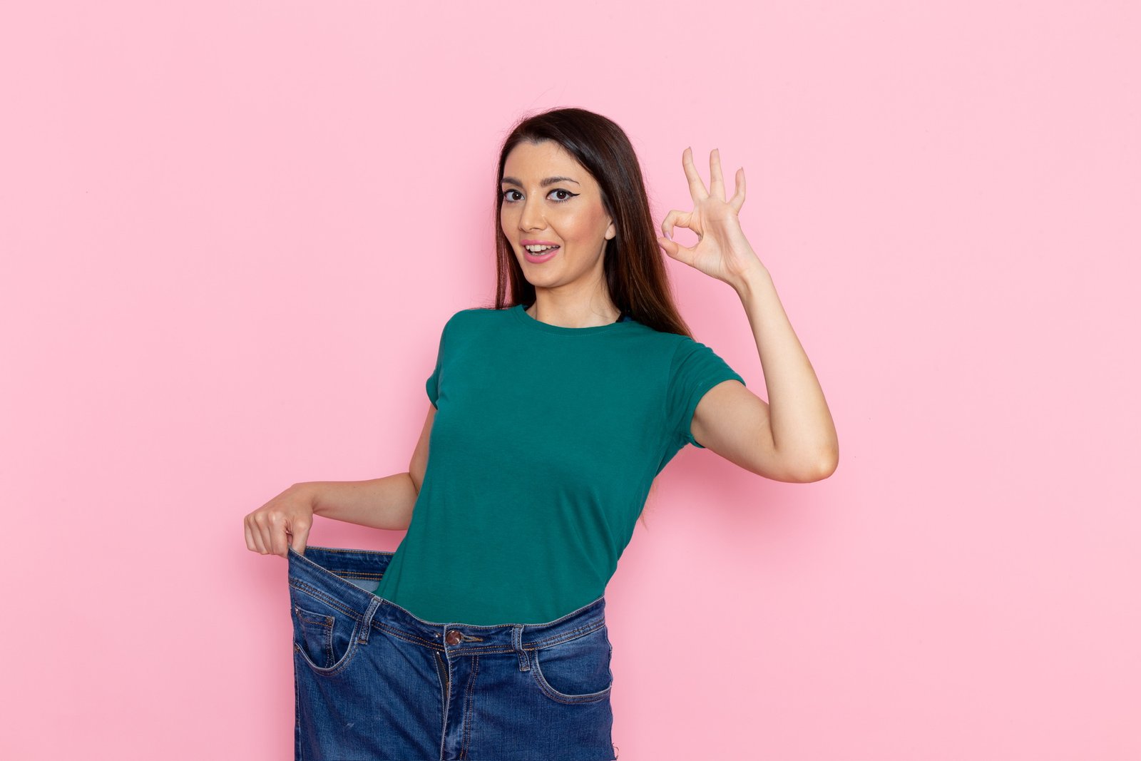 front view young female in green t shirt showing her slim body on the pink background waist sport exercise workout beauty slim athlete